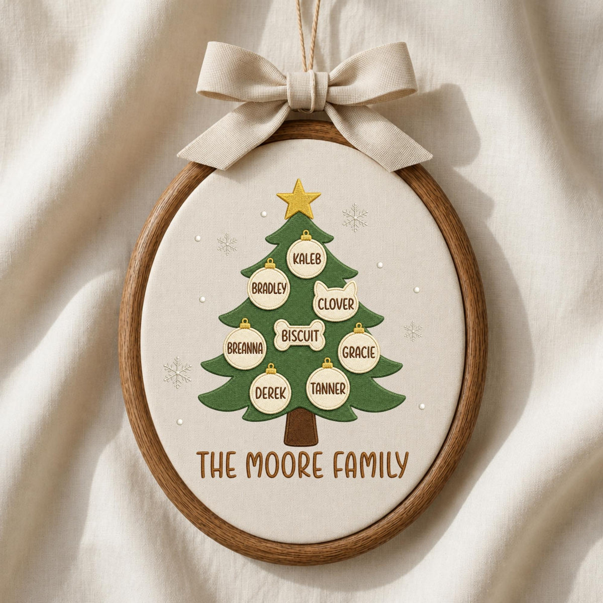 May include: An oval embroidery hoop ornament featuring a green Christmas tree with a gold star, decorated with white ornaments labeled with the names Kaleb, Bradley, Clover, Biscuit, Breanna, Gracie, Derek, and Tanner, with the text THE MOORE FAMILY.