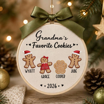 May include: A round embroidery hoop ornament featuring a dark olive green satin ribbon bow at the top. The fabric center displays the embroidered text Grandma's Favorite Cookies, two gingerbread figures, a paw print, and the year 2026.