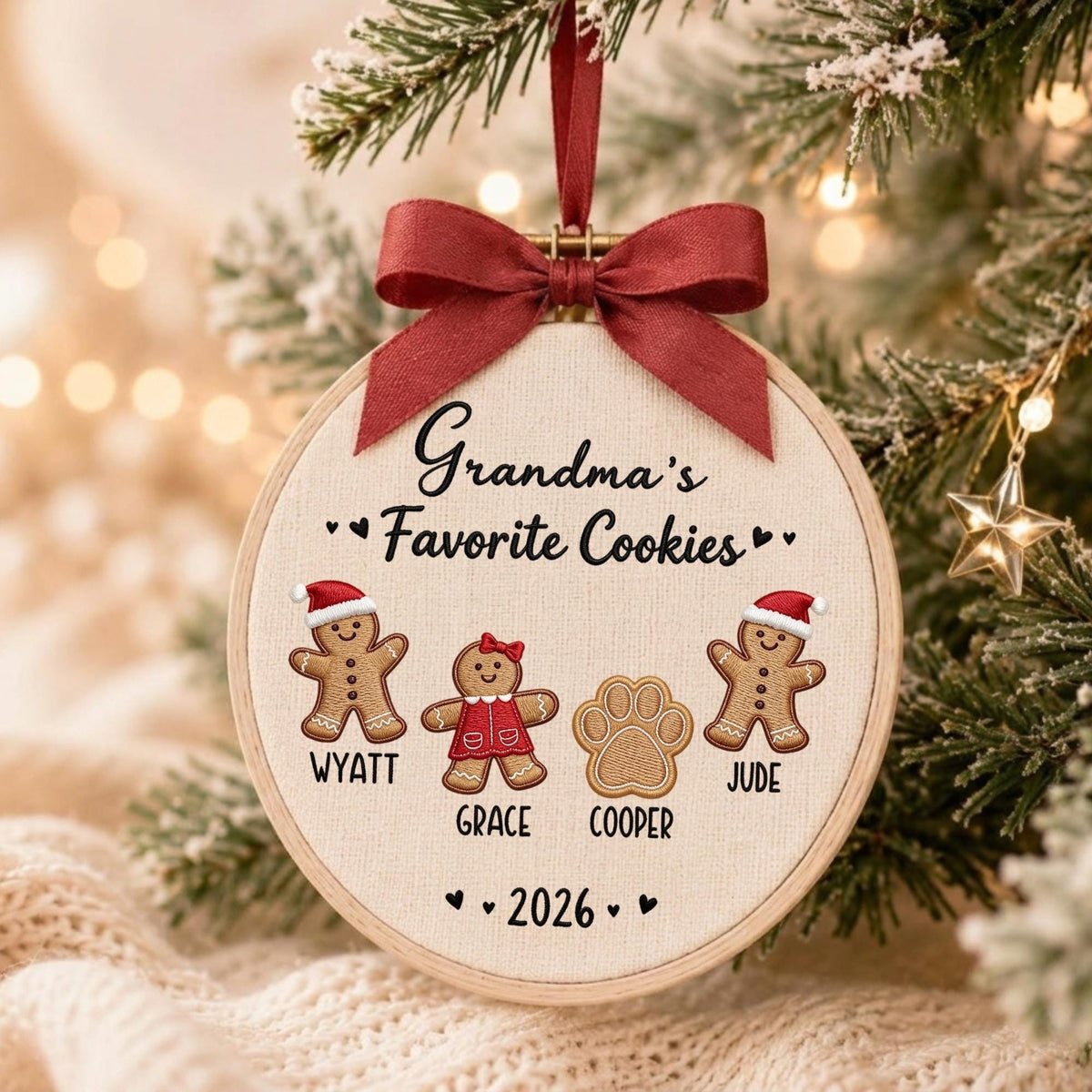 May include: A round wooden embroidery hoop ornament featuring cream fabric with the embroidered text Grandma's Favorite Cookies. It includes gingerbread figures named Wyatt, Grace, and Jude, a paw print named Cooper, and the year 2026, topped with a dark red ribbon.