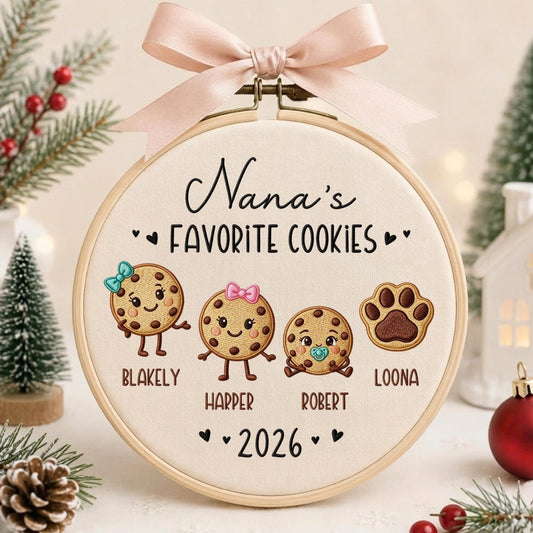 May include: A round wooden embroidery hoop featuring cream fabric with the embroidered text Nana's FAVORITE COOKIES and 2026. It displays three cookie characters with names Blakely, Harper, Robert, and a paw print labeled Loona, topped with a pink bow.