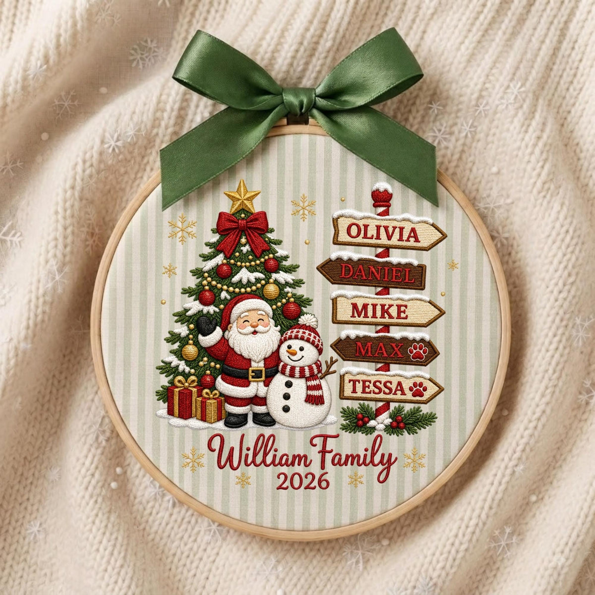 May include: A round embroidery hoop ornament featuring a Christmas tree, Santa Claus, and a snowman. A green ribbon bow sits at the top. A signpost displays the names Olivia, Daniel, Mike, Max, and Tessa. The text reads William Family 2026.