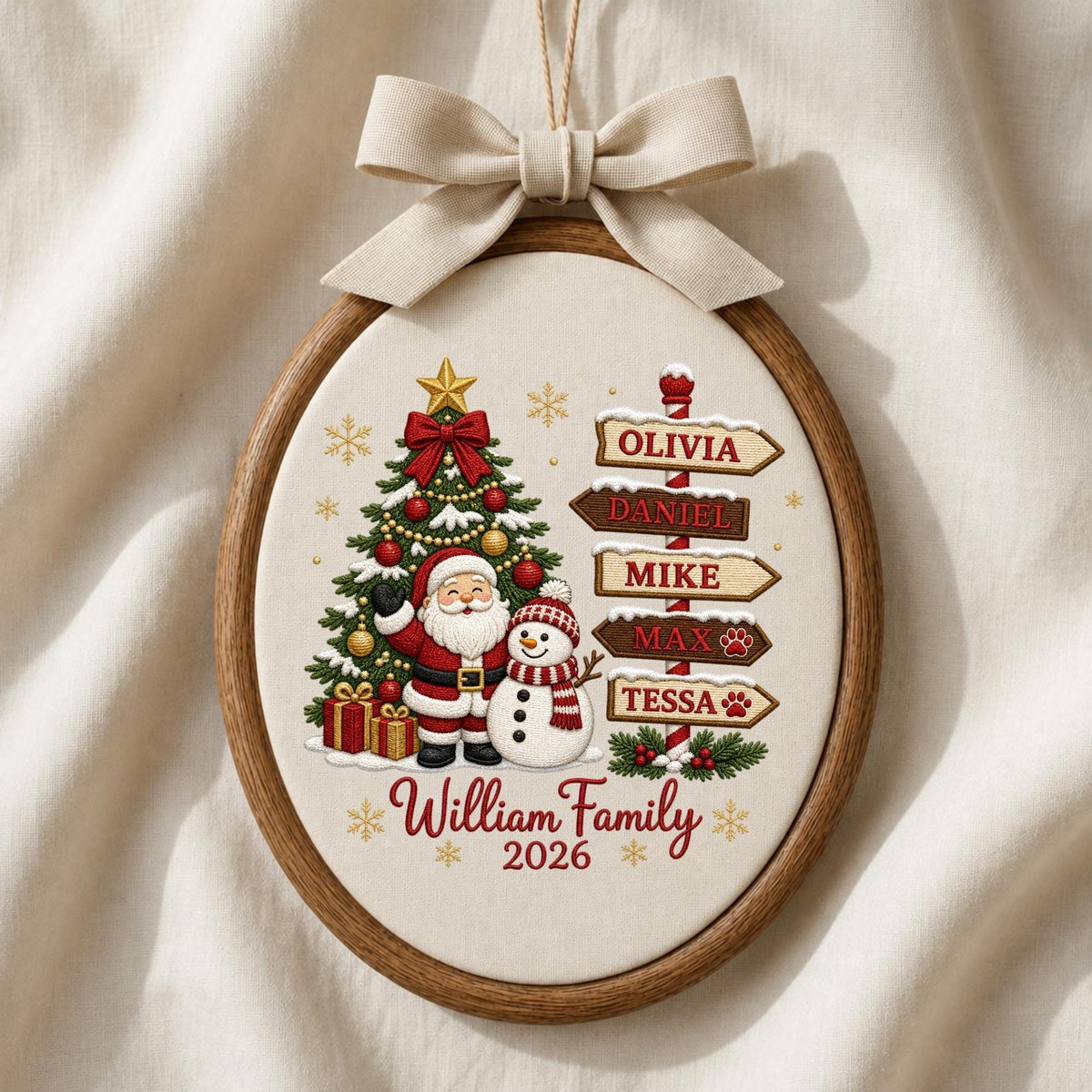 May include: An oval wooden embroidery hoop ornament featuring a cream fabric background with a printed Christmas scene of Santa Claus, a snowman, and a tree. A signpost lists the names Olivia, Daniel, Mike, Max, and Tessa. Text reads William Family 2026.