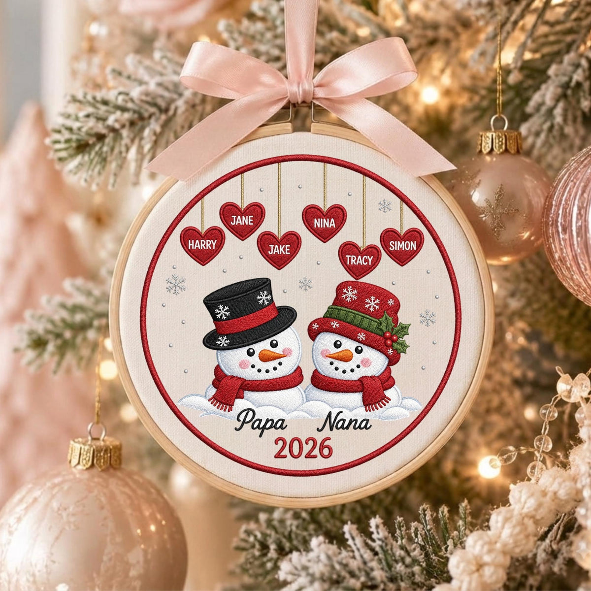 May include: A round wooden embroidery hoop ornament featuring two snowmen with red scarves and hats, one with a black top hat. Above them are six red hearts with the names Jane, Nina, Harry, Jake, Tracy, and Simon. Text reads Papa Nana 2026.