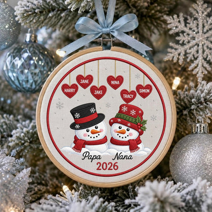 May include: A round wooden embroidery hoop ornament featuring two embroidered snowmen wearing hats and scarves. Above them, six red hearts are embroidered with the names Jane, Nina, Harry, Jake, Tracy, and Simon. The text Papa Nana 2026 is below.