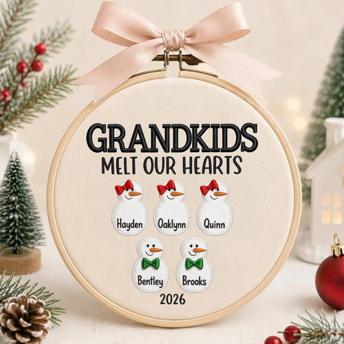 May include: A round wooden embroidery hoop containing cream fabric with the black embroidered text GRANDKIDS MELT OUR HEARTS. It features five white snowman figures with orange noses, red bows or green bow ties, and names embroidered below.