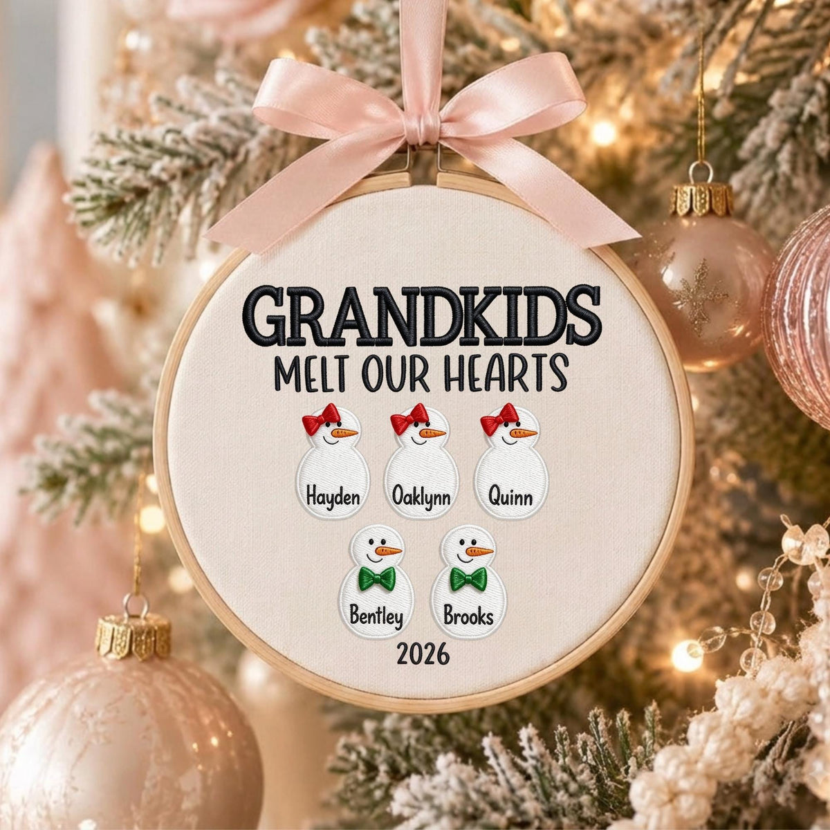 May include: A round wooden embroidery hoop ornament featuring cream fabric with the black embroidered text GRANDKIDS MELT OUR HEARTS. It displays five embroidered snowman figures with names Hayden, Oaklynn, Quinn, Bentley, and Brooks, plus 2026.