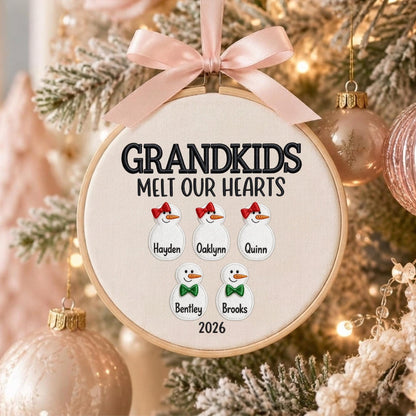 May include: A round wooden embroidery hoop ornament featuring cream fabric with the black embroidered text GRANDKIDS MELT OUR HEARTS. It displays five embroidered snowman figures with names Hayden, Oaklynn, Quinn, Bentley, and Brooks, plus 2026.