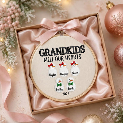 May include: A round wooden embroidery hoop containing cream fabric with the embroidered text GRANDKIDS MELT OUR HEARTS. Five snowman figures are stitched below, labeled Hayden, Oaklynn, Quinn, Bentley, and Brooks, with the year 2026 below.