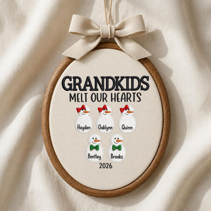May include: An oval wooden embroidery hoop ornament featuring the embroidered text GRANDKIDS MELT OUR HEARTS and 2026. It displays five white snowman figures with names Hayden, Oaklynn, Quinn, Bentley, and Brooks, topped with a beige fabric bow.