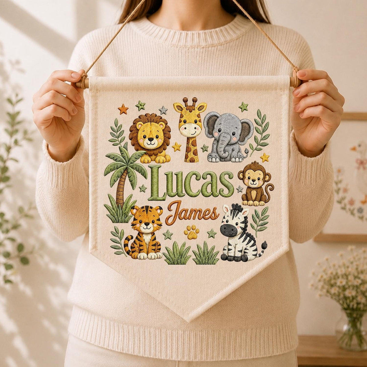 May include: A cream-colored fabric wall banner featuring a printed jungle theme with a lion, giraffe, elephant, monkey, tiger, and zebra. The text Lucas James is printed in the center, surrounded by green palm trees, leaves, and small stars.