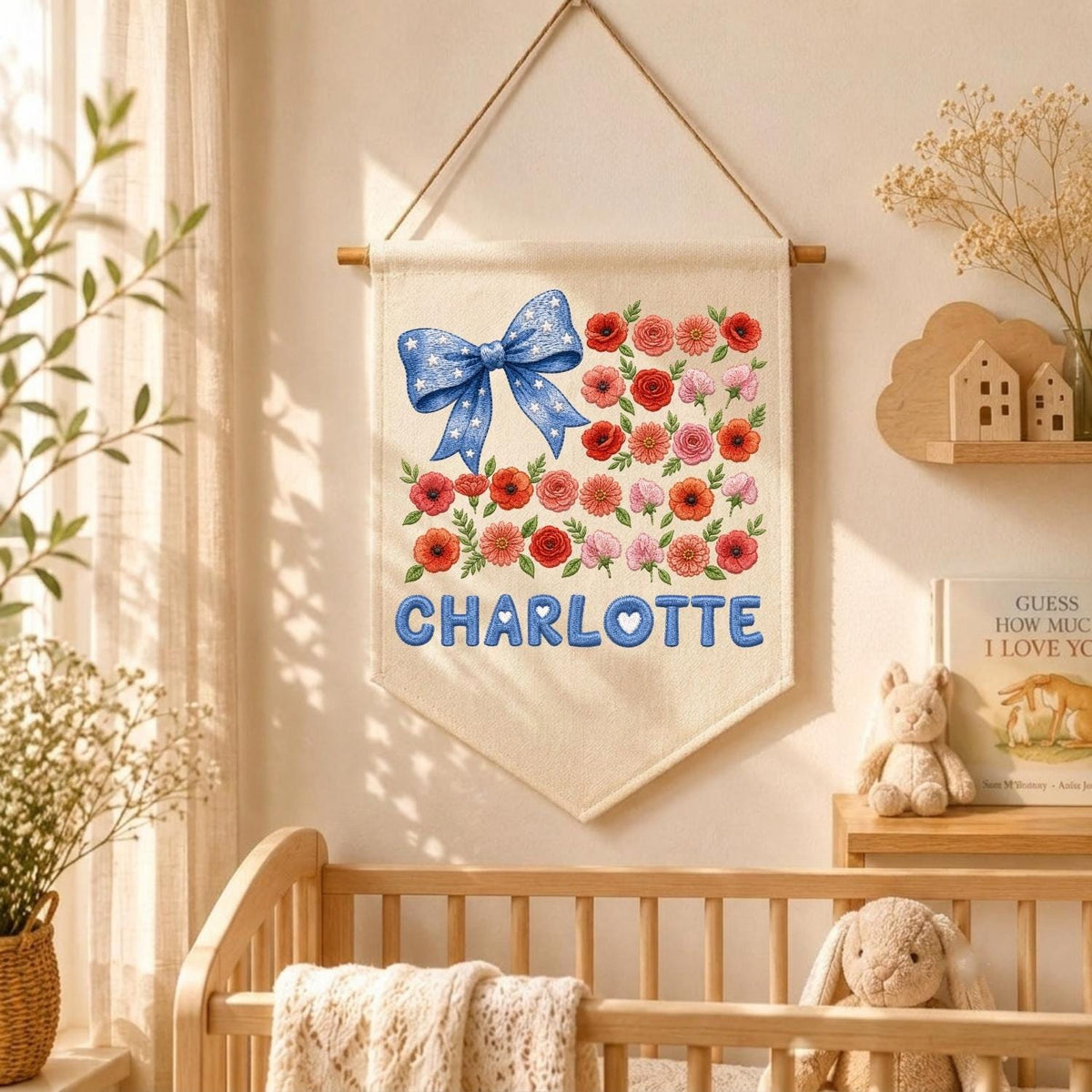 May include: A cream-colored fabric wall hanging banner featuring a blue bow with white stars on the left and a cluster of red, orange, and pink flowers on the right. The name CHARLOTTE is printed in large blue letters at the bottom of the banner.