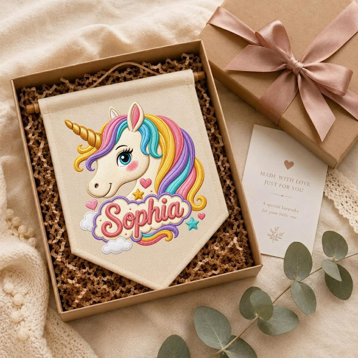 May include: A cream-colored fabric wall banner featuring an embroidered unicorn with a gold horn and a multi-colored mane. The name Sophia is embroidered in pink script below the unicorn, surrounded by small stars, hearts, and clouds.