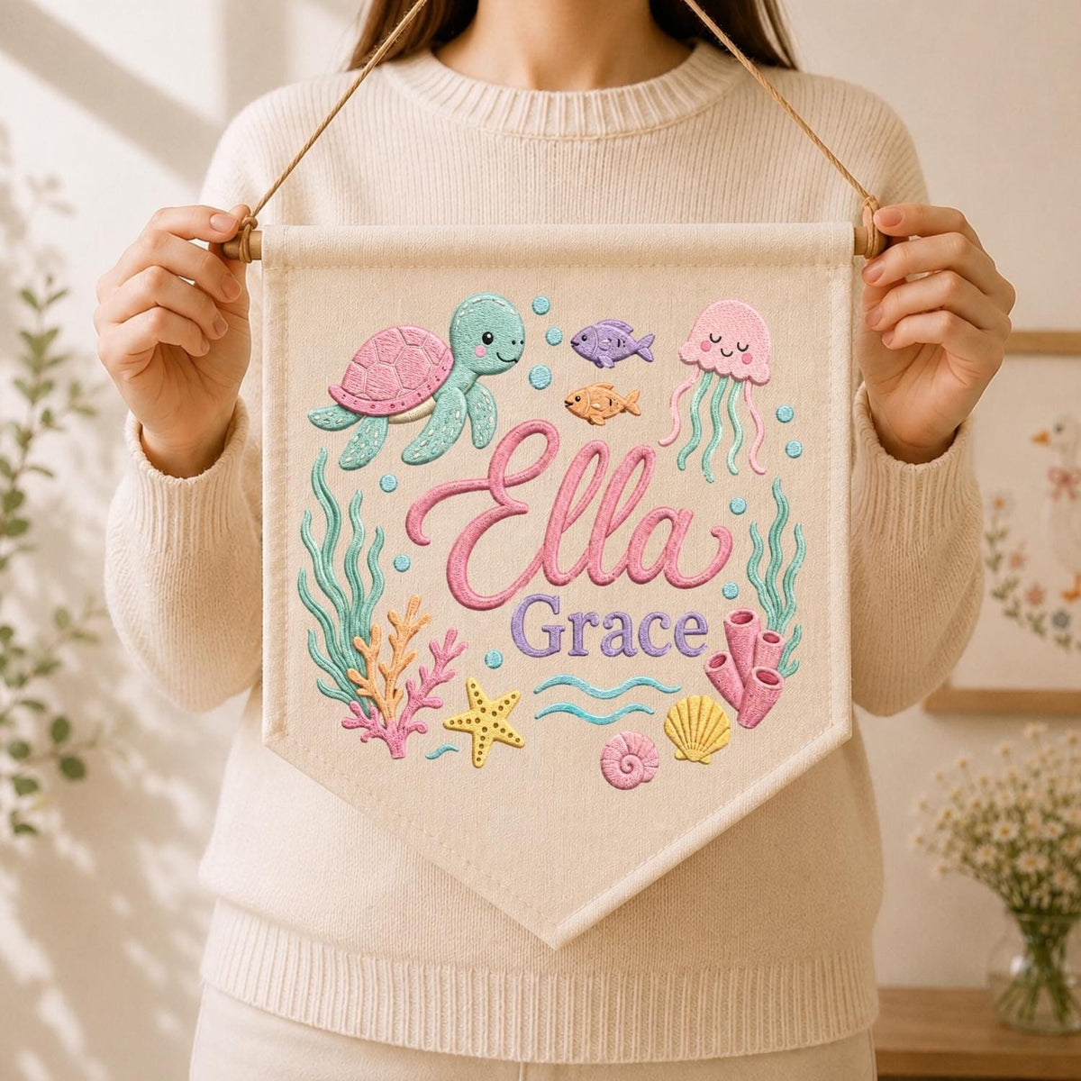 May include: A cream-colored fabric wall banner featuring a colorful underwater scene with a sea turtle, jellyfish, starfish, coral, and shells. The name Ella Grace is printed in the center in a pink script font with purple block lettering.