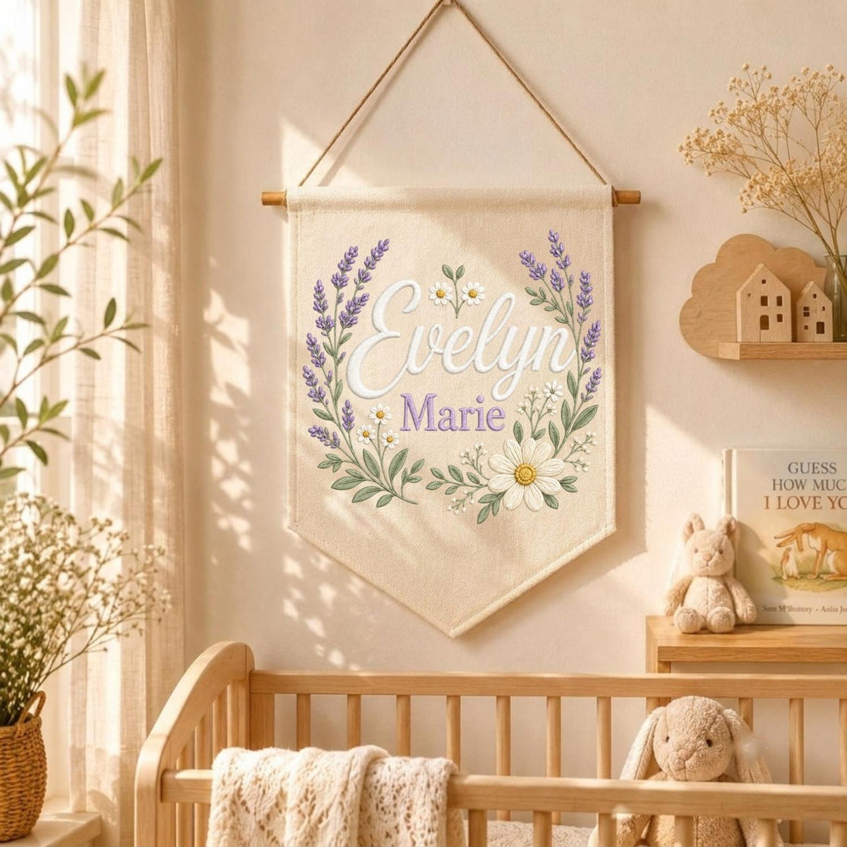 May include: A cream-colored fabric wall banner featuring the name Evelyn Marie in white and purple script. The text is surrounded by a printed botanical wreath of purple lavender sprigs and white daisies, suspended from a wooden dowel with a cord.