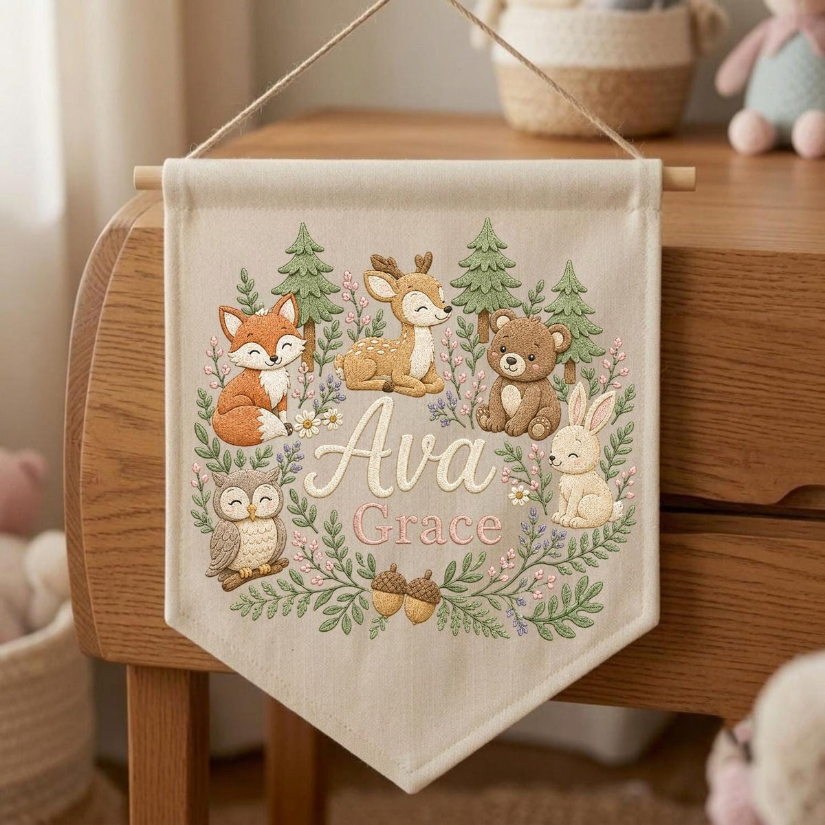May include: A beige fabric wall banner featuring a woodland theme with a fox, deer, bear, owl, and rabbit surrounded by green pine trees and flowers. The name Ava Grace is printed in the center in a decorative script and block font.