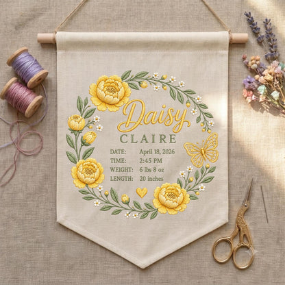 May include: A beige fabric wall hanging featuring an embroidered wreath of yellow flowers and green leaves. The text reads Daisy CLAIRE, DATE: April 18, 2026, TIME: 2:45 PM, WEIGHT: 6 lbs 8 oz, LENGTH: 20 inches, with a small yellow heart and butterfly.