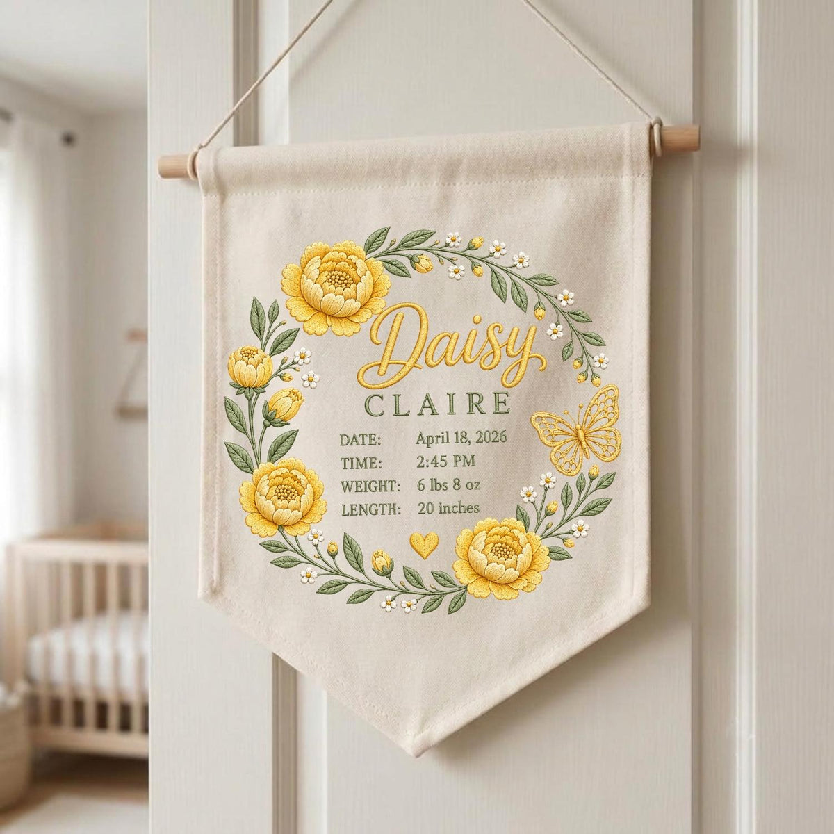 May include: A cream-colored fabric wall banner featuring a yellow floral wreath with green leaves and a butterfly. The text reads Daisy CLAIRE, DATE: April 18, 2026, TIME: 2:45 PM, WEIGHT: 6 lbs 8 oz, LENGTH: 20 inches, with a small yellow heart icon.