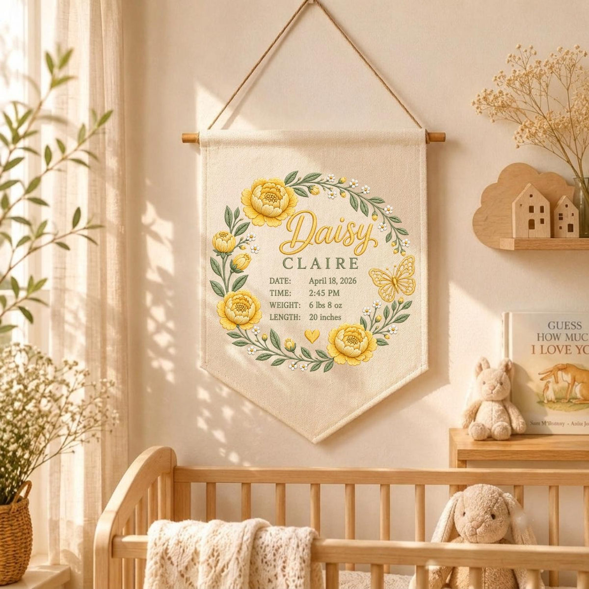 May include: A cream-colored fabric wall hanging featuring a yellow floral wreath, a butterfly, and the name Daisy Claire. The text includes the date April 18, 2026, time 2:45 PM, weight 6 lbs 8 oz, and length 20 inches, all suspended from a wooden rod.