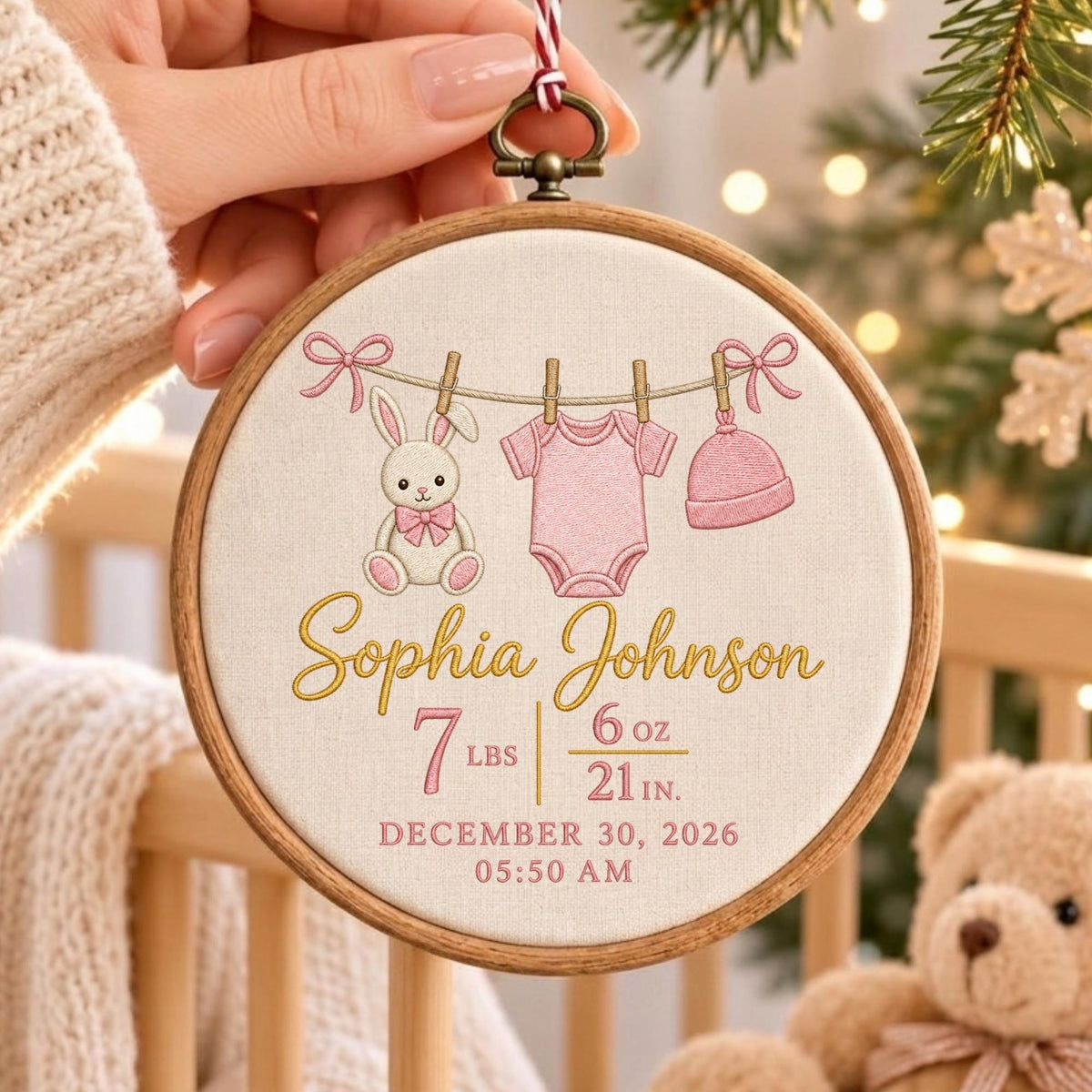 May include: A round wooden embroidery hoop featuring a cream fabric background with an embroidered clothesline displaying a pink bunny, a pink baby bodysuit, and a pink hat. The text reads Sophia Johnson, 7 lbs 6 oz, 21 in, December 30, 2026, 05:50 AM.