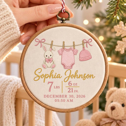 May include: A round wooden embroidery hoop featuring a cream fabric background with an embroidered clothesline displaying a pink bunny, a pink baby bodysuit, and a pink hat. The text reads Sophia Johnson, 7 lbs 6 oz, 21 in, December 30, 2026, 05:50 AM.