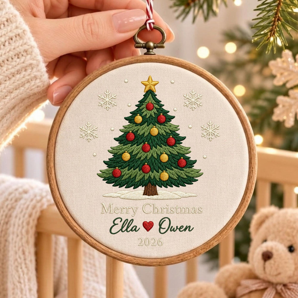 May include: A round wooden embroidery hoop containing off-white fabric with a stitched green Christmas tree, red and yellow ornaments, a gold star, and white snowflakes. The text reads Merry Christmas, Ella, a red heart, Owen, and 2026.