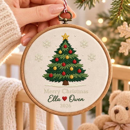May include: A round wooden embroidery hoop containing off-white fabric with a stitched green Christmas tree, red and yellow ornaments, a gold star, and white snowflakes. The text reads Merry Christmas, Ella, a red heart, Owen, and 2026.