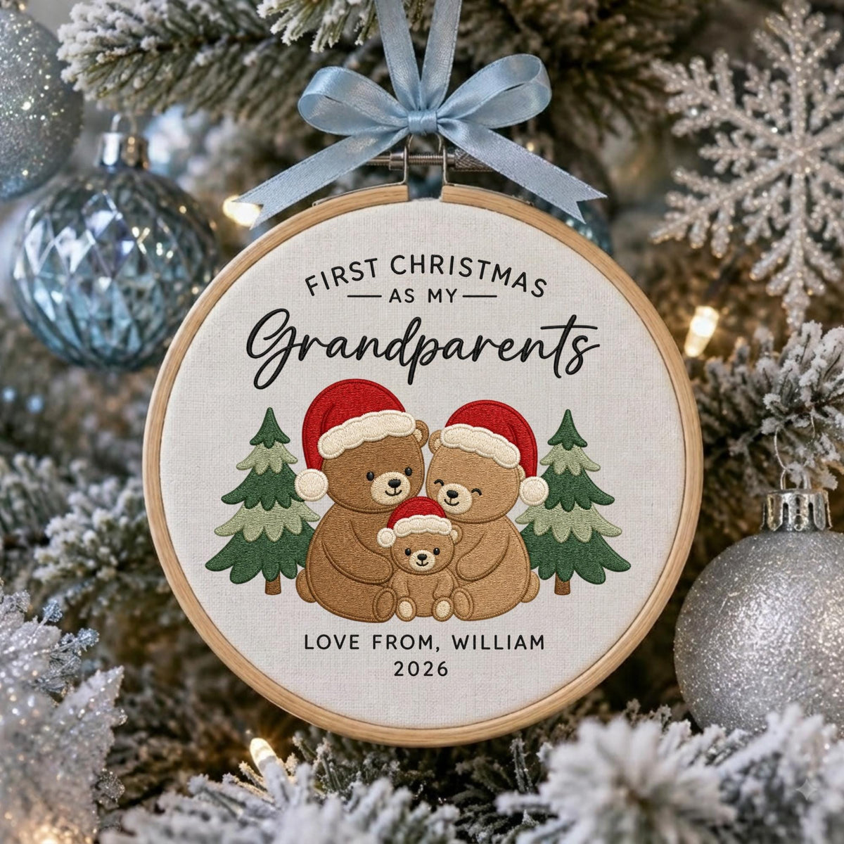 May include: A round wooden embroidery hoop ornament featuring a light-colored fabric center with embroidered text reading FIRST CHRISTMAS AS MY Grandparents, LOVE FROM, WILLIAM, 2026, and three brown bears in red Santa hats between two green pine trees.