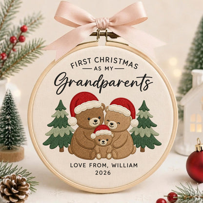 May include: A round wooden embroidery hoop containing cream fabric with an embroidered design of three brown bears wearing red Santa hats. The text reads FIRST CHRISTMAS AS MY Grandparents, LOVE FROM, WILLIAM, 2026. A light pink ribbon is tied at the top.