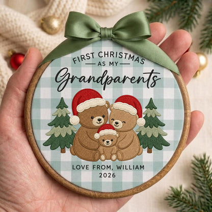 May include: A round wooden embroidery hoop ornament featuring a light blue and white buffalo check fabric. The design includes three embroidered teddy bears wearing red Santa hats, two green pine trees, and the text "FIRST CHRISTMAS AS MY Grandparents" and "LOVE FROM, WILLIAM 2026". A sage green satin ribbon is tied at the top.