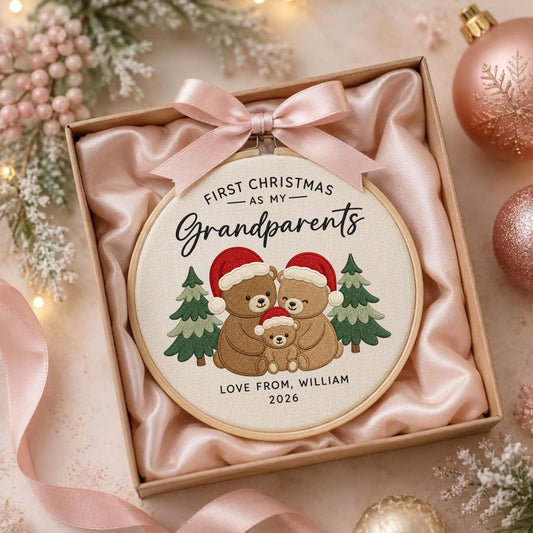 May include: A round embroidery hoop featuring a cream fabric background with three brown bears wearing red Santa hats, flanked by two green pine trees. The text reads: FIRST CHRISTMAS AS MY Grandparents LOVE, WILLIAM 2026. A pink satin ribbon is tied at the top.