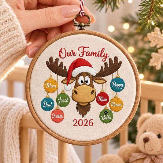 May include: A round wooden embroidery hoop ornament featuring a tan moose wearing a red and white Santa hat. The text Our Family and 2026 are embroidered in red. Eight colorful ornaments hang from the moose antlers with names Mom, Dad, Charlotte, Jacob, Mimi, Memaw, Poppy, and Bella.