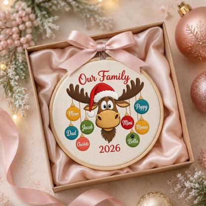 May include: A round embroidery hoop ornament featuring a cartoon moose wearing a Santa hat, with the text Our Family and 2026. Hanging from the moose antlers are colorful ornaments labeled Mom, Dad, Charlotte, Jacob, Poppy, Mimi, Memaw, and Bella.