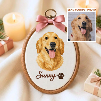 May include: An oval wooden embroidery hoop containing a fabric panel with a golden retriever portrait, the name Sunny, and a paw print. A pink satin ribbon bow is attached to the top metal hanger. An inset shows a photo of a golden retriever.