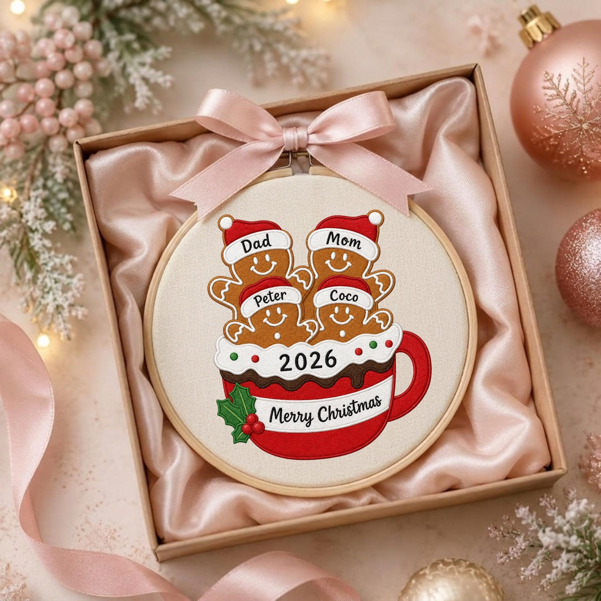 May include: A circular embroidery hoop featuring a stitched design of four gingerbread figures in a red mug. The figures are labeled Dad, Mom, Peter, and Coco, all wearing Santa hats. The mug displays the text 2026 and Merry Christmas.