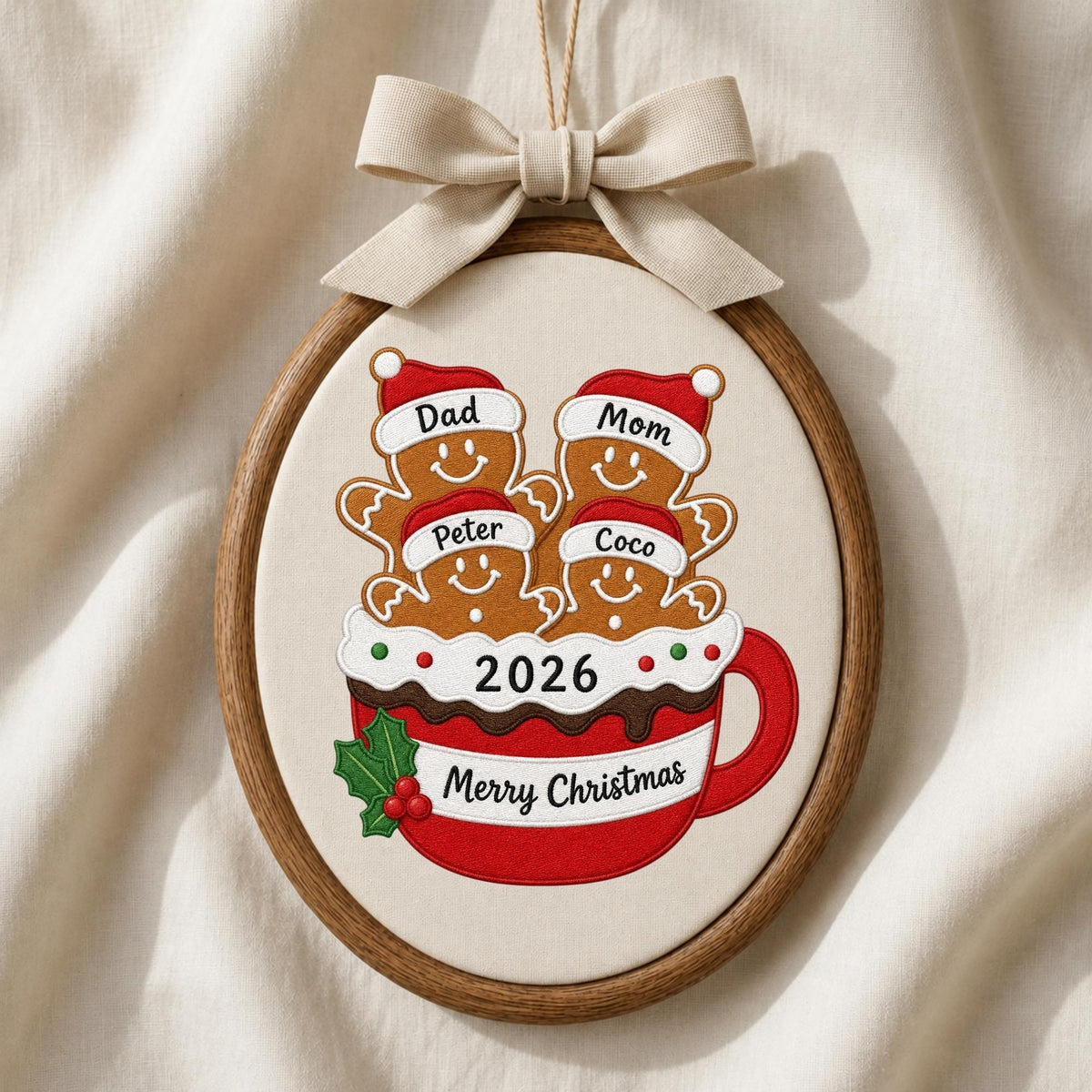 May include: An oval embroidery hoop ornament featuring a red mug filled with four gingerbread figures wearing Santa hats labeled Dad, Mom, Peter, and Coco. The mug displays the text 2026 and Merry Christmas, accented by a holly sprig and a beige bow.