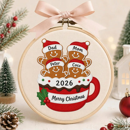 May include: A round wooden embroidery hoop containing fabric with an embroidered design of four gingerbread people in a red mug. The gingerbread figures wear Santa hats labeled Dad, Mom, Peter, and Coco. The mug features the text 2026 and Merry Christmas.