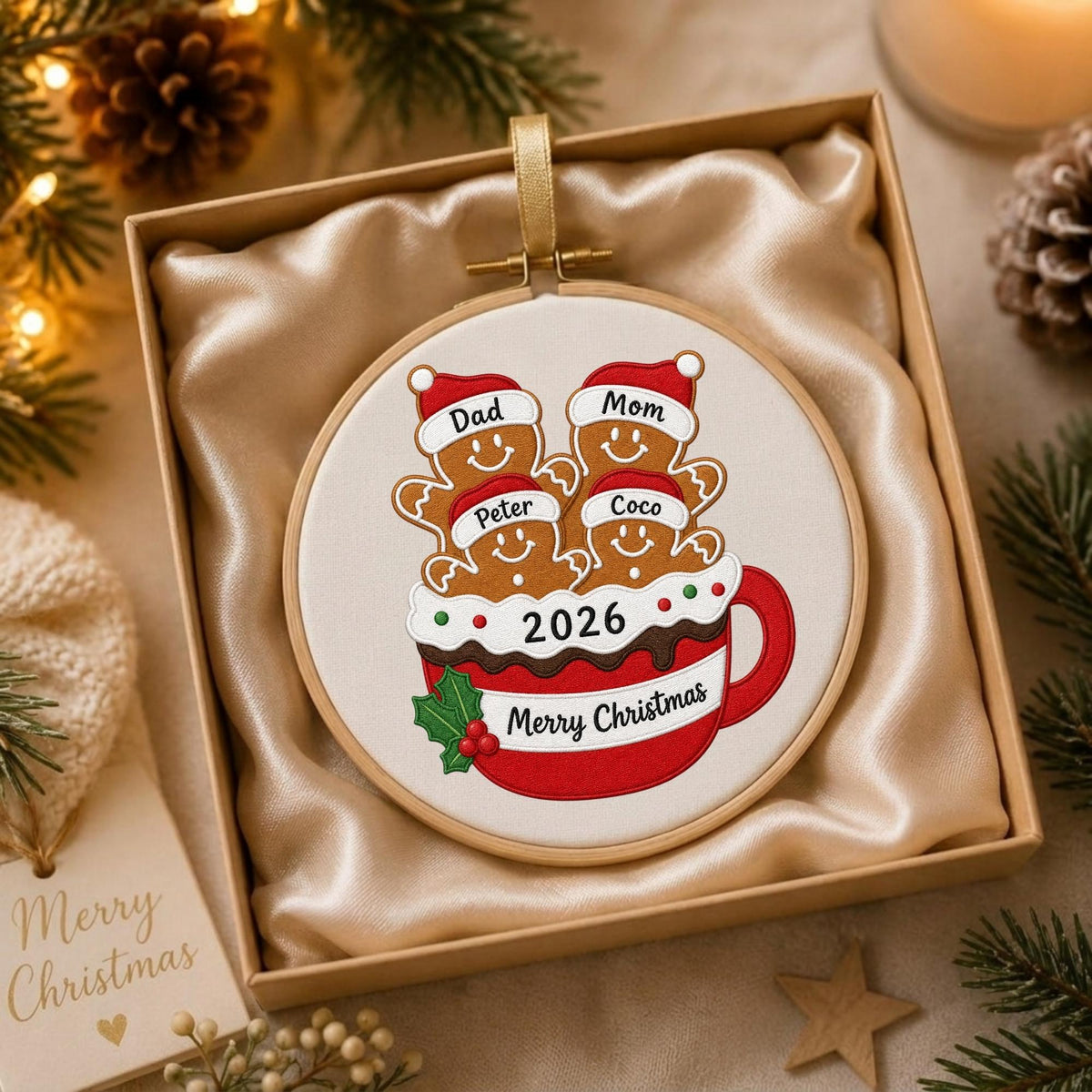 May include: A round wooden embroidery hoop ornament featuring a white fabric center with an embroidered red mug filled with four gingerbread figures wearing Santa hats labeled Dad, Mom, Peter, and Coco. The mug displays the text 2026 and Merry Christmas.