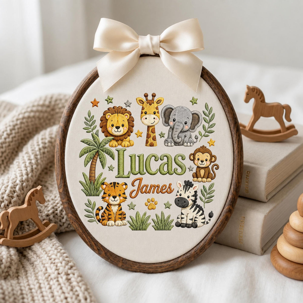 May include: An oval embroidery hoop with a dark wood frame and a cream fabric center. The fabric features embroidered jungle animals including a lion, giraffe, elephant, monkey, tiger, and zebra, with the names Lucas James and a palm tree.