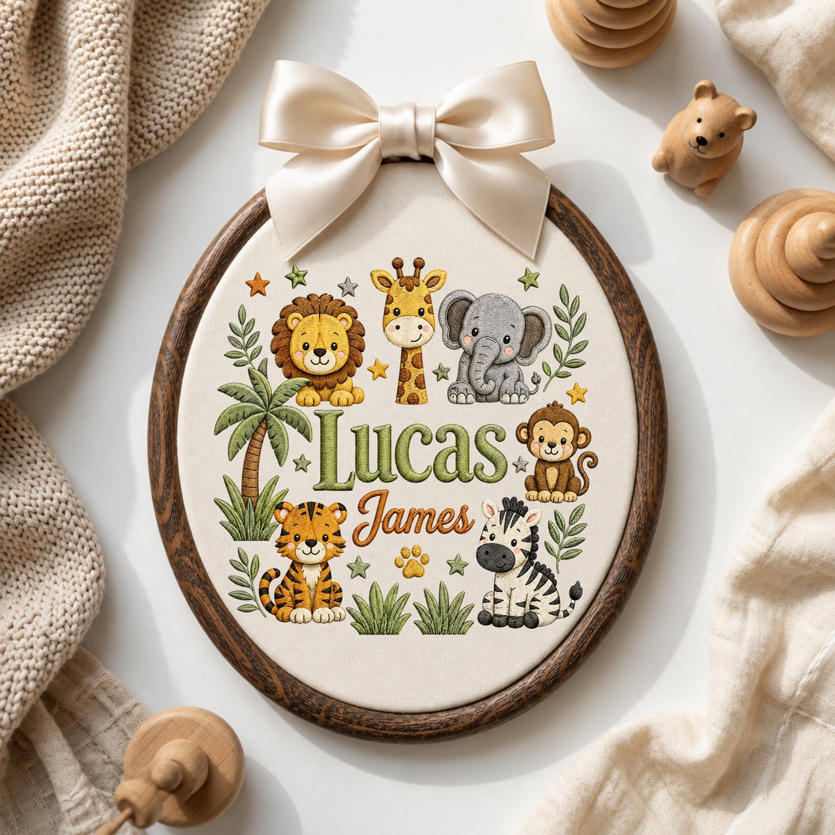May include: An oval embroidery hoop featuring a cream fabric background with a dark wood frame and a cream satin bow. The design includes embroidered illustrations of a lion, giraffe, elephant, monkey, tiger, and zebra, with the name Lucas James.
