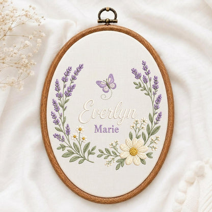 May include: An oval wooden embroidery hoop containing white fabric with hand-stitched floral embroidery. The design features lavender sprigs, white daisies, and a purple butterfly surrounding the embroidered names Everlyn and Marie in script.