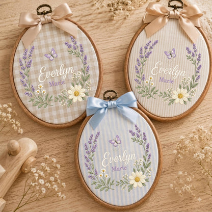 May include: Three oval wooden embroidery hoops featuring fabric backgrounds with gingham or striped patterns. Each hoop displays embroidered lavender, daisies, a butterfly, and the name Everlyn Marie in white and purple script, topped with a satin bow.