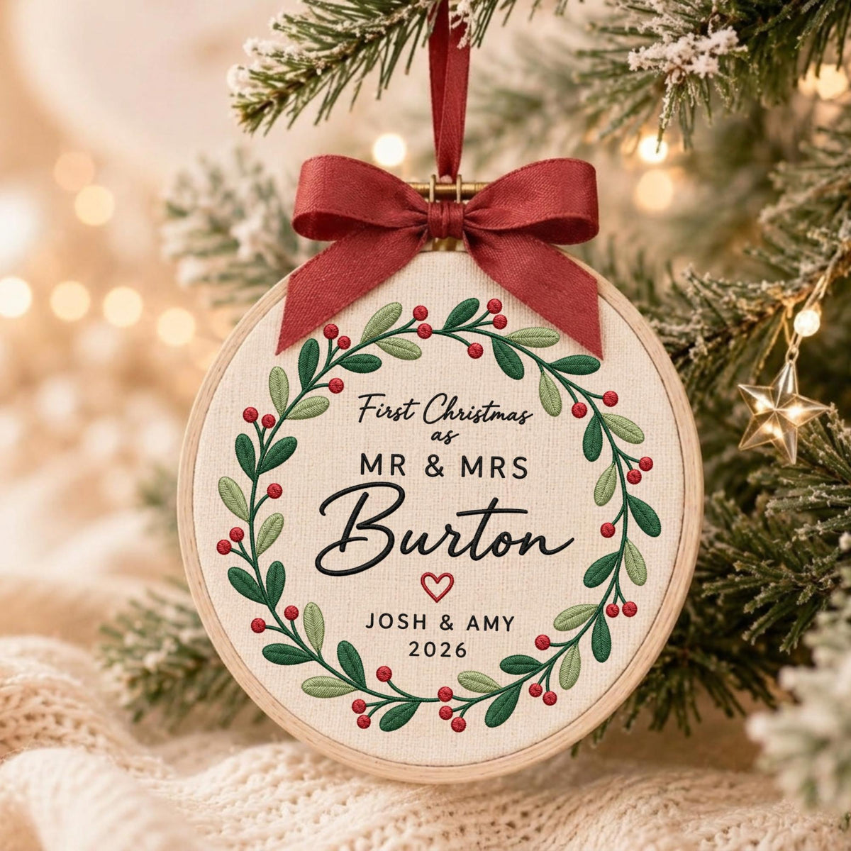 May include: A round wooden embroidery hoop ornament featuring a cream fabric center with an embroidered green leaf and red berry wreath. The text reads First Christmas as MR &amp; MRS Burton with a small red heart, JOSH &amp; AMY, and 2026.