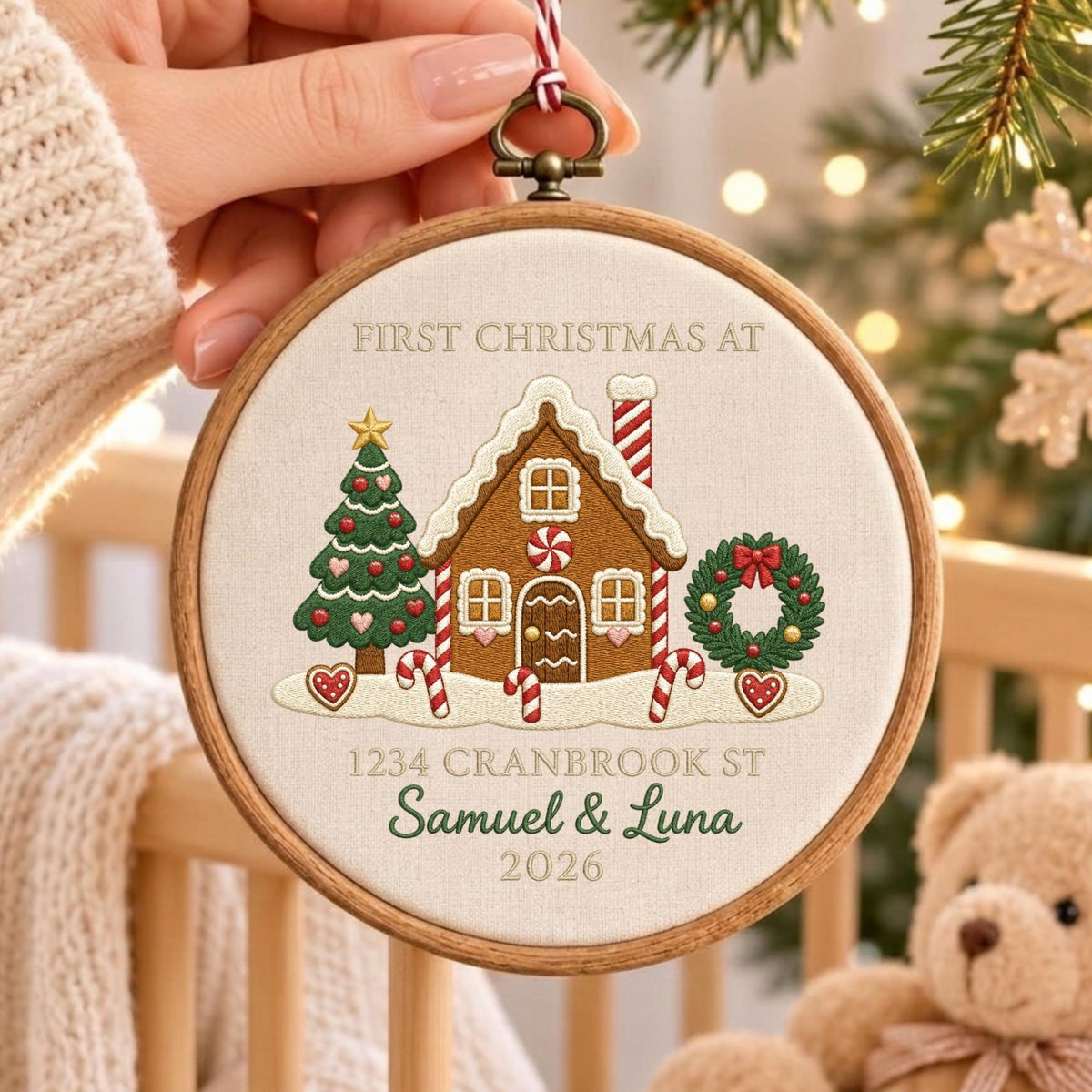 May include: A round wooden embroidery hoop containing fabric with an embroidered gingerbread house, a Christmas tree, and a wreath. The text reads FIRST CHRISTMAS AT, 1234 CRANBROOK ST, Samuel &amp; Luna, and 2026. It features red and white candy canes.