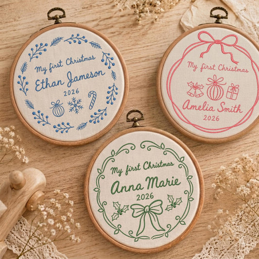 May include: Three circular wooden embroidery hoops containing white fabric with personalized Christmas designs. Each hoop features the text My first Christmas, a name, and the year 2026, embroidered in blue, pink, or green thread with festive motifs.