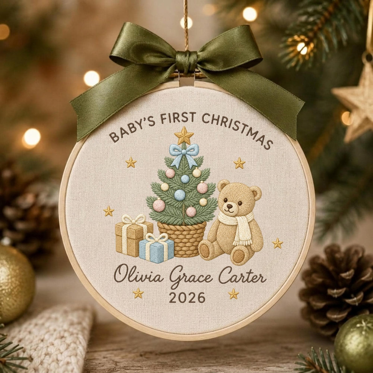 May include: A round embroidery hoop ornament featuring a beige fabric background with a green ribbon bow at the top. The design includes a Christmas tree, a teddy bear, gifts, and the text Baby's First Christmas, Olivia Grace Carter, and 2026.