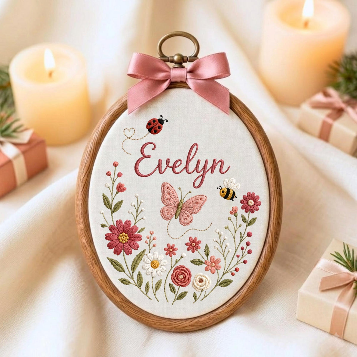 May include: An oval wooden embroidery hoop containing white fabric with the name Evelyn stitched in pink cursive. The design features a pink butterfly, a ladybug, a bee, and various colorful floral stems in shades of pink, red, and green.
