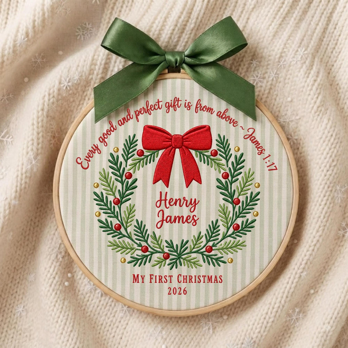 May include: A circular embroidery hoop featuring a light green and white striped fabric with a green satin bow at the top. The design includes a red bow, a green wreath with red berries, and the text "Every good and perfect gift is from above ~ James 1:17", "Henry James", "MY FIRST CHRISTMAS", and "2026".