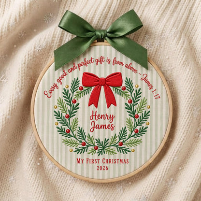 May include: A circular embroidery hoop featuring a light green and white striped fabric with a green satin bow at the top. The design includes a red bow, a green wreath with red berries, and the text "Every good and perfect gift is from above ~ James 1:17", "Henry James", "MY FIRST CHRISTMAS", and "2026".