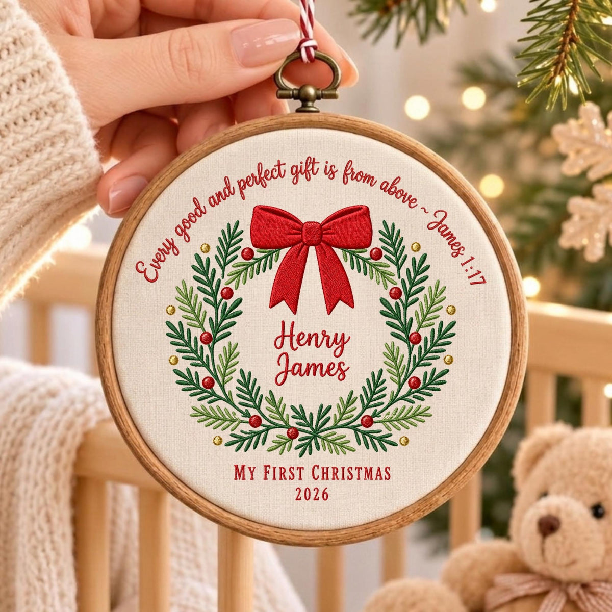 May include: A round wooden embroidery hoop containing white fabric with a stitched green wreath, red berries, and a red bow. Text reads: Every good and perfect gift is from above ~ James 1:17, Henry James, MY FIRST CHRISTMAS 2026.