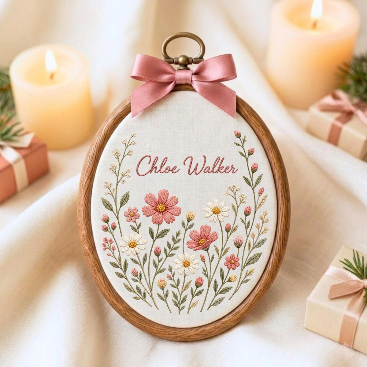 May include: An oval wooden embroidery hoop containing white fabric with the embroidered name Chloe Walker in pink script, surrounded by a floral arrangement of pink and white flowers with green stems, topped with a pink satin ribbon bow.